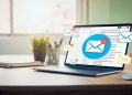 Computadora portátil en un escritorio con iconos de correos electrónicos flotando, ilustrando email marketing.