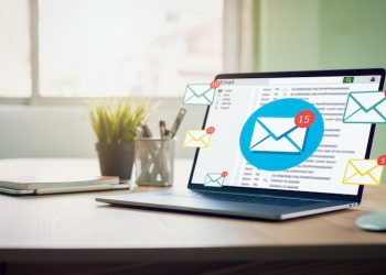 Computadora portátil en un escritorio con iconos de correos electrónicos flotando, ilustrando email marketing.