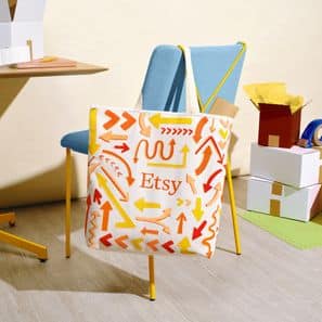 Bolsa de tela estampada con patrones y logo de Etsy, en una sala con sillas azules y cajas.