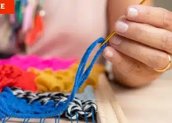 Mano tejiendo con lana azul en un telar de colores con etiqueta 'Free' en la esquina.