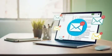 Computadora portátil en un escritorio con iconos de correos electrónicos flotando, ilustrando email marketing.