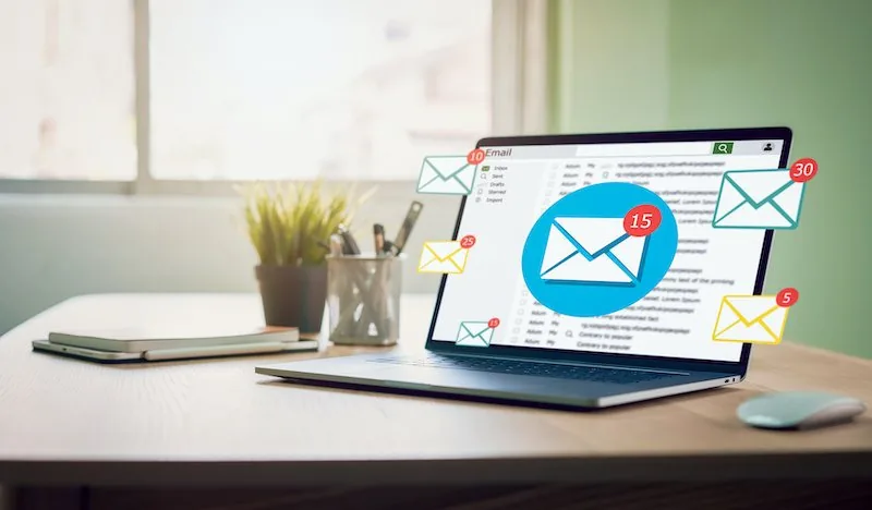 Computadora portátil en un escritorio con iconos de correos electrónicos flotando, ilustrando email marketing.