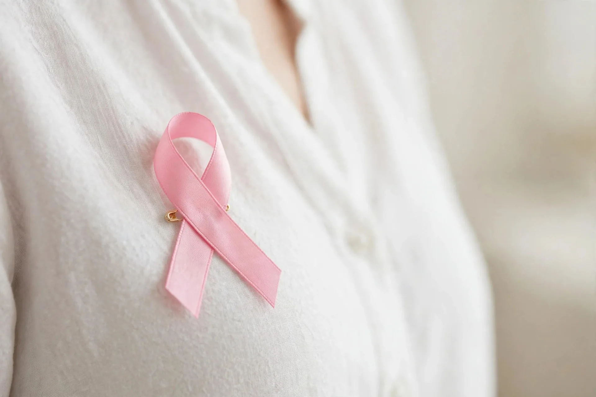 Mujer joven con un lazo rosa prendido en la solapa de su chaqueta sonriendo a cámara