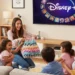Una familia de cinco miembros se sienta en un sofá, ríen y comparten palomitas mientras ven juntos Disney+ en un acogedor salón. Una mujer sostiene una manta de colores y los niños sonríen entusiasmados.
