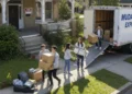 Cinco jóvenes trasladan cajas y muebles de un camión rotulado "Mudanzas Express" a una casa con un cartel de Se Alquila, subiendo las pertenencias por la pasarela y la rampa en un día soleado.