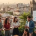 Un grupo de jóvenes profesionales colabora en una azotea con vistas a la ciudad. Discuten cerca de una pantalla que muestra una presentación empresarial con el logotipo "Starps". Al fondo se ven exuberantes plantas y edificios históricos.