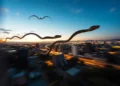 Imagen surrealista de serpientes voladoras sobre una ciudad al atardecer, con movimiento borroso en el fondo.